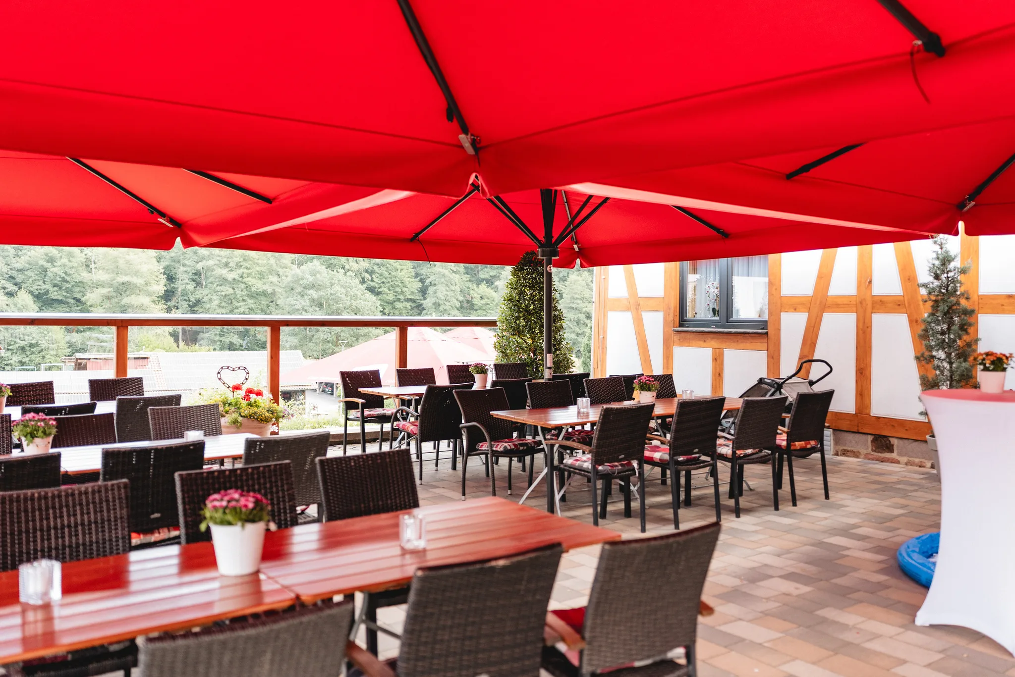 Gedeckte Tische unter einem großen roten Sonnenschirm auf einer Terrasse in Kleinlüder bei einer Hochzeitsfeier.