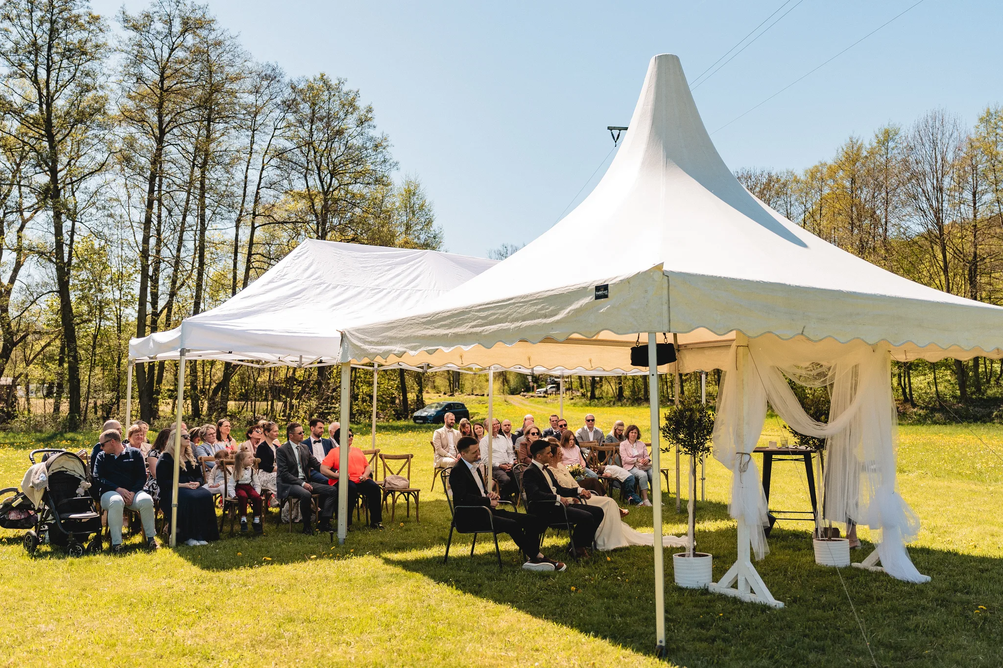 Gäste und Trauplätze unter weißen Pavillons auf einer Wiese vor Bäumen.