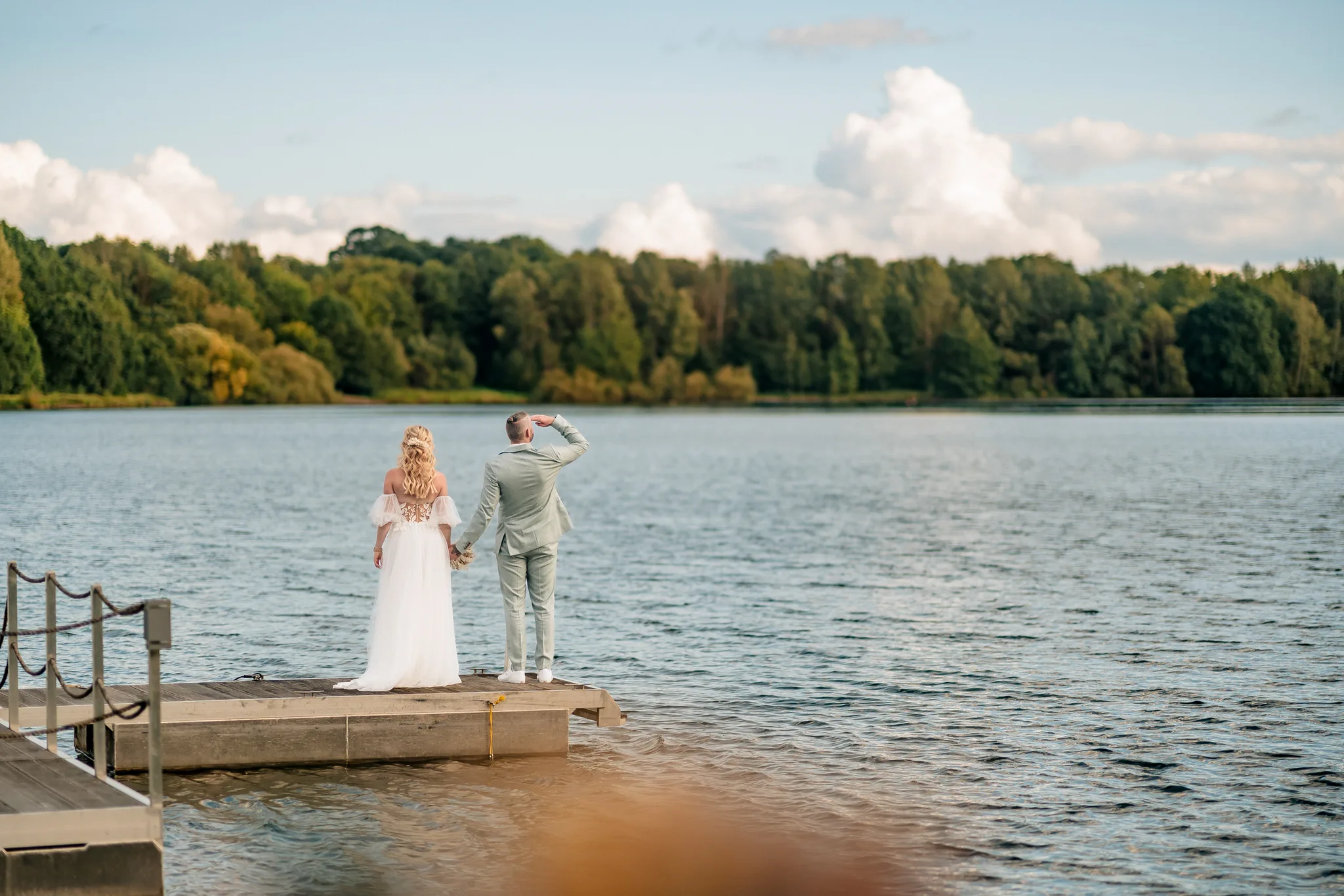 Das Brautpaar steht händchenhaltend auf einem Holzsteg und blickt über den See am Lakeside Resort Michaela.